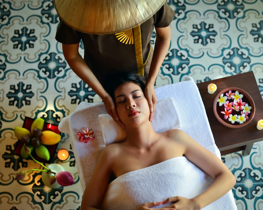 Kỹ thuật viên đội nón lá massage đầu cho khách trong phòng lát gạch bông